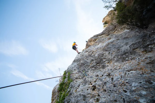 驚くほど晴れた日に山の壁を登る男性登山者のショットの下から — ストック写真