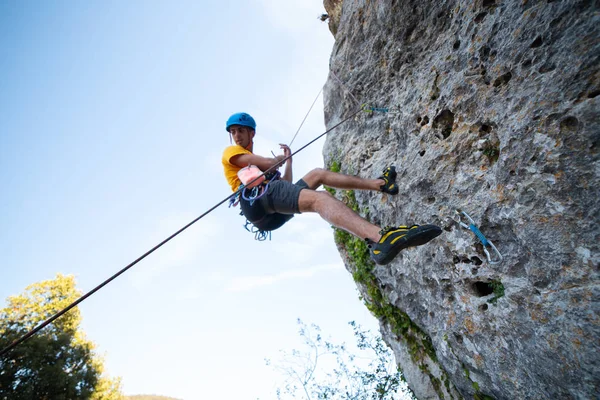 From below shot of male climber climbing mountain wall on amazing sunny day