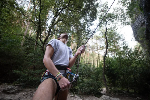 From below of man with rope on rock looking up checking another climber before going up