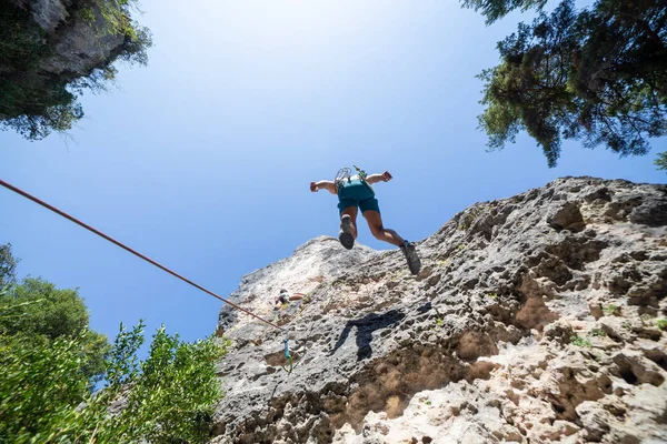 Young man climbing down the mountain doing rappel a sunny day