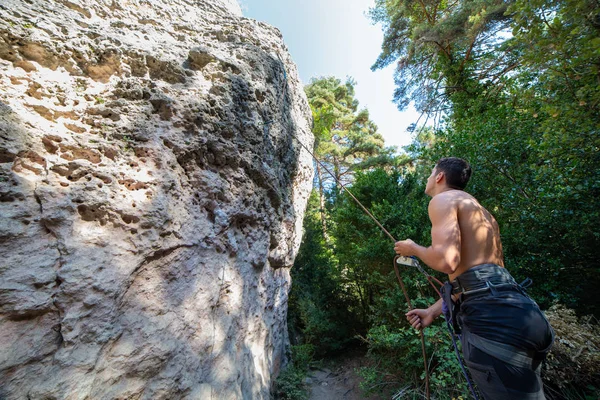 From below of man with rope on rock looking up checking another climber before going up