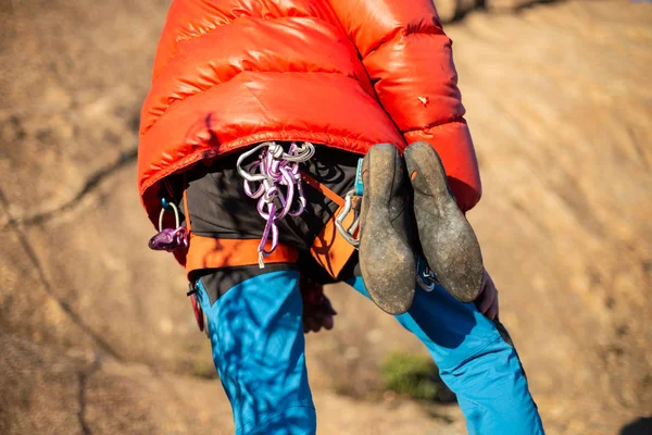 From below shot of man in warm coat looking up and checking climbing partner on high cliff in sunlight