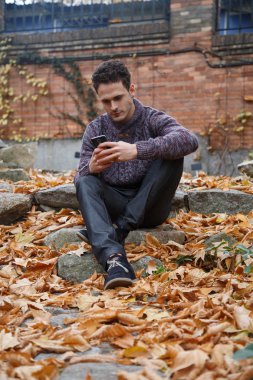 Genç yakışıklı bir rock ile yeşillik çayır üzerinde oturan ve smartphone ile konuşan adam