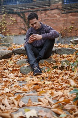 Genç yakışıklı bir rock ile yeşillik çayır üzerinde oturan ve smartphone ile konuşan adam