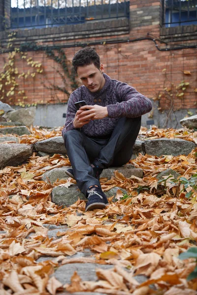 Genç yakışıklı bir rock ile yeşillik çayır üzerinde oturan ve smartphone ile konuşan adam