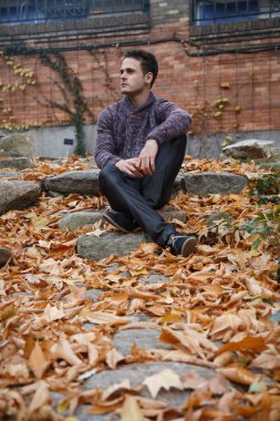 Çayır bitki örtüsü ile bir kaya üzerinde oturan genç yakışıklı adam