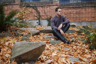 Çayır bitki örtüsü ile bir kaya üzerinde oturan genç yakışıklı adam