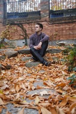 Çayır bitki örtüsü ile bir kaya üzerinde oturan genç yakışıklı adam