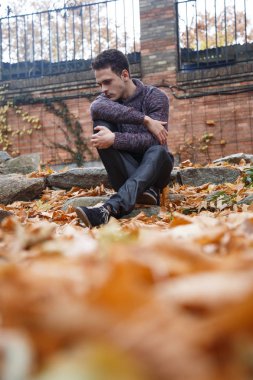 Çayır bitki örtüsü ile bir kaya üzerinde oturan genç yakışıklı adam