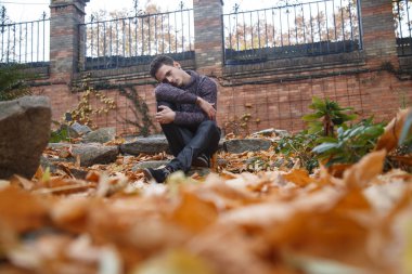 Çayır bitki örtüsü ile bir kaya üzerinde oturan genç yakışıklı adam