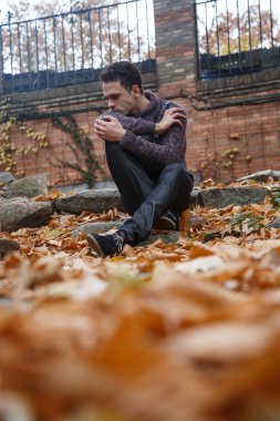 Çayır bitki örtüsü ile bir kaya üzerinde oturan genç yakışıklı adam