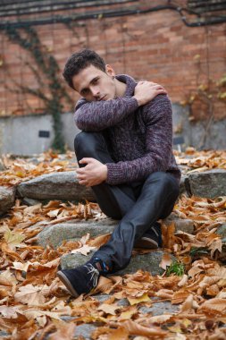 Çayır bitki örtüsü ile bir kaya üzerinde oturan genç yakışıklı adam