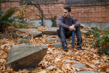 Çayır bitki örtüsü ile bir kaya üzerinde oturan genç yakışıklı adam