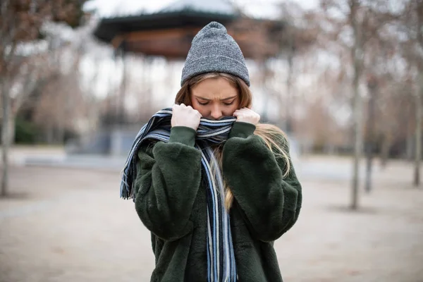 在非常寒冷的日子里 穿着温暖衣服的漂亮年轻女性穿着围巾包裹着 把目光移开 同时站在秋天公园模糊的背景上 — 图库照片