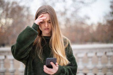 Alin sürtünme ve sonbahar park dururken modern smartphone bakarak sorunlu genç kadın