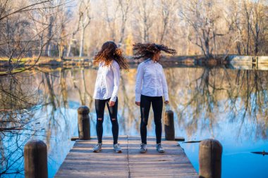 Ormanda sonbahar günü aynı kıyafetleri giyen genç ikiz kız kardeşler gölde saç sallıyorlar.