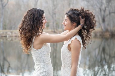 Sakin gölde gülümseyen ve sonbahar günü birbirlerine saç tarayan neşeli ikiz kız kardeşlerin yan görünümü