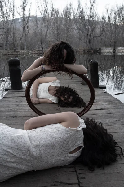 在秋日的秋天 在平静的湖畔的木码头上 穿着同样白色衣服的双胞胎与镜子合影 — 图库照片