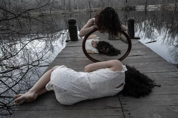 在秋日的秋天 在平静的湖畔的木码头上 穿着同样白色衣服的双胞胎与镜子合影 — 图库照片