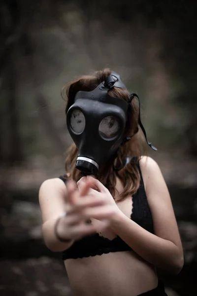 Portrait of anonymous woman in black clothes and gas mask standing in amazing spooky forest