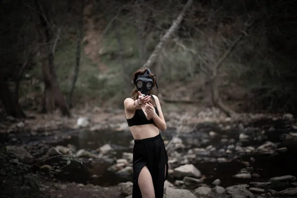 匿名赤脚妇女穿着黑色衣服和防毒面具站在惊人的怪异森林侧视图 — 图库照片