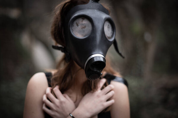 Portrait of anonymous woman in black clothes and gas mask standing in amazing spooky forest