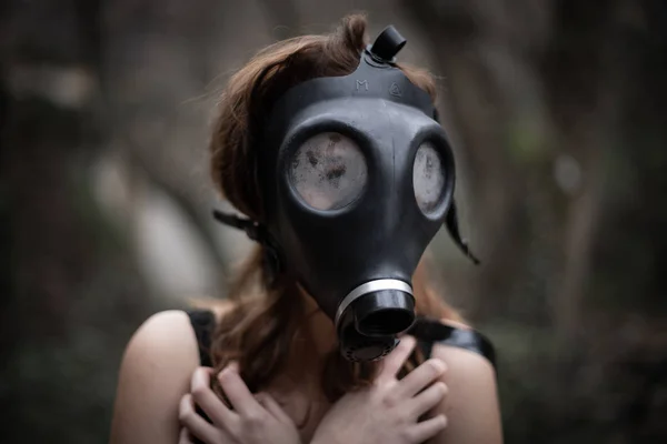 Portrait of anonymous woman in black clothes and gas mask standing in amazing spooky forest