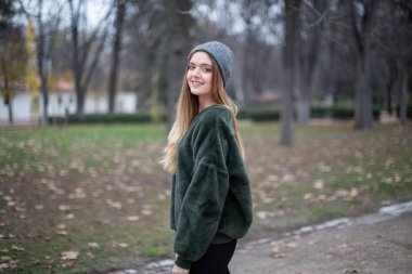 Sonbaharda bir parkta kış şapkalı mutlu gülümseyen genç sarışın kadın Portresi
