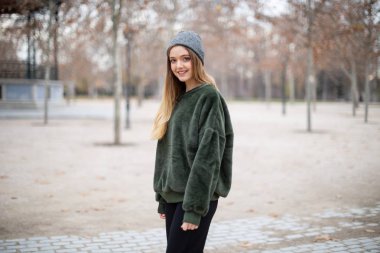 Sonbaharda bir parkta kış şapkalı mutlu gülümseyen genç sarışın kadın Portresi