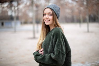 Sonbaharda bir parkta kış şapkalı mutlu gülümseyen genç sarışın kadın Portresi