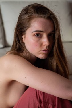 Kahverengi saçlı genç üstsüz sevimli kadın portresi yerde oturan ve kameraya bakarak