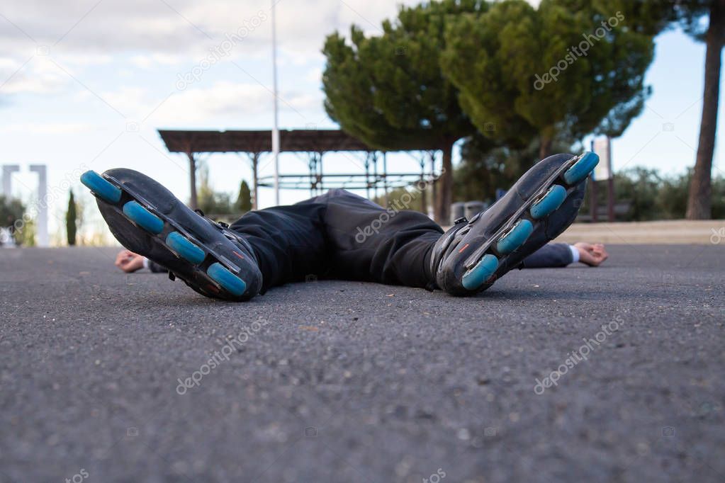 Young fit weary man in sportswear with roller skates lying on road in beautiful city park