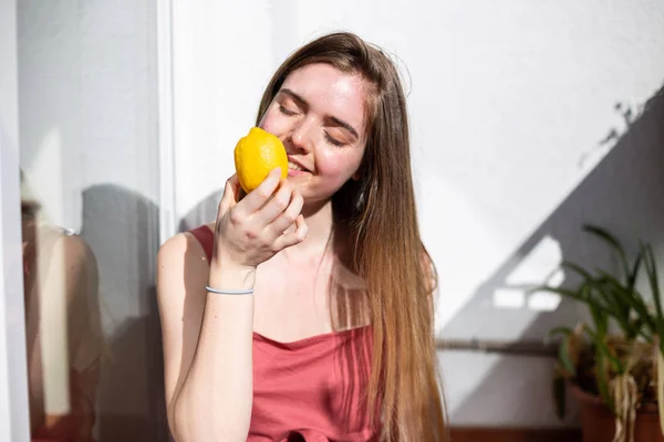 Genç, mutlu, yaz elbisesi içinde terasta oturan ve gözlerini olgun limonlarla kaplayan bir kadın.