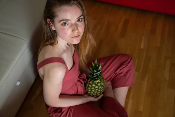 年轻疲惫的女性 拿着菠萝坐在地板上 — 图库照片