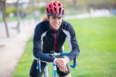 Spor ve kask parkta Bisiklete oturan ve kamera bakarak Genç uygun erkek bisikletçi gülümseyen