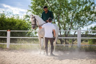 Genç adam çiftlikte bulutlu bir günde siyah adama çayırda ata binmeyi öğretiyor.