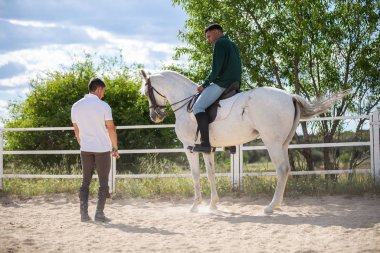 Genç adam çiftlikte bulutlu bir günde siyah adama çayırda ata binmeyi öğretiyor.