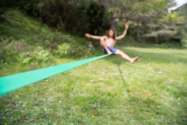 夏の日にフィールドでスラックラインをやって裸の胴子を持つデフォーカスの若者 — ストック写真