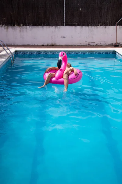 Anonymous young man floating in a inflatable flamingo in a large blue pool on a sunny holiday day