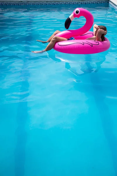 Young man floating in a inflatable flamingo in a blue pool a sunny day of summer vacation