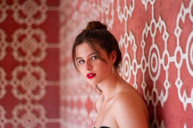 Beyaz süslemeli pembe tasarım duvara yaslanmış ve kameraya bakan genç güzel kadın portresi