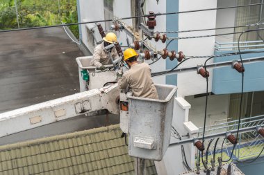 Üniformalı elektrikçiler bir elektrik hattını tamir ediyor. Tamir kamyonunun havalandırma platformunda çalışıyorlar..