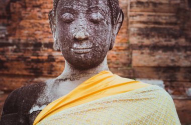 Buda, huzur dolu, meditasyon yapan yüzü ve gözleri kapalı, Ayutthaya 'daki Wat Mahathat' da turuncu bezle kaplanmış parçalanmış bir heykel. Tayland sanatı. Unesco Dünya Mirası Sitesi.