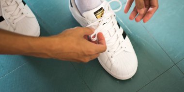 Bangkok, Tayland - 20 Mayıs 2019: Bir adam beyaz Adidas Superstar spor ayakkabıları bağlıyor.