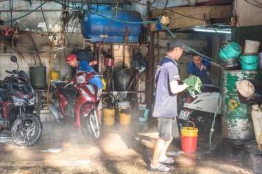 Ho Chi Minh City, Vietnam - 9 Ocak 2019: 3 adam Saigon 'un basit insanlarının günlük yaşamı ve çalışmaları için küçük, pejmürde bir motosiklet yıkama yerinde çalışıyor..