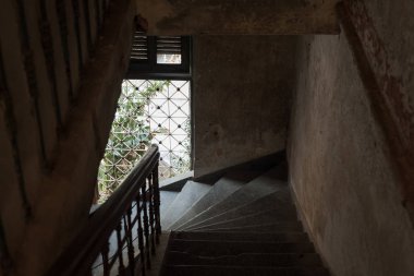 Parmaklıklı bir pencereden gelen doğal ışığın olduğu eski bir evde karanlık bir merdiven iniyor. Konak ya da Villa Bodega, Phnom Penh, Kamboçya.