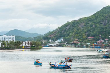 Nha Trang, Vietnam - 5 Mayıs 2018: Cai Nehri balıkçı mavisi botları, Cham Oasis Condotel & Villas 'ı barındıran bir ada ve kıyıları boyunca evleri ve tapınakları olan kayalık ağaçlık bir dağ.