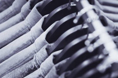 Row of denim jackets or shirts on black hangers, a top view closeup. Jeans wardrobe. Blue textile background, blurry (shallow depth of field). clipart