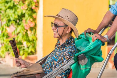 Hoi An, Vietnam - 23 Ekim 2018: Güneş gözlüklü ve şapkalı mutlu bir Asyalı gezgin, arka planda eski kasabanın tipik sarı renginde bir duvarı olan triportörün kabininde oturuyor..