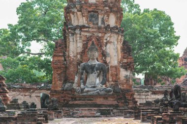 Ayutthaya, Tayland 'daki Wat Phra Mahathat' da (Mahatat) oturan Buda. Madalyalı bir tuğla kule harabeleri ve antik bir Budist tapınağının heykeli gökyüzüne ve ağaç yapraklarına karşı..